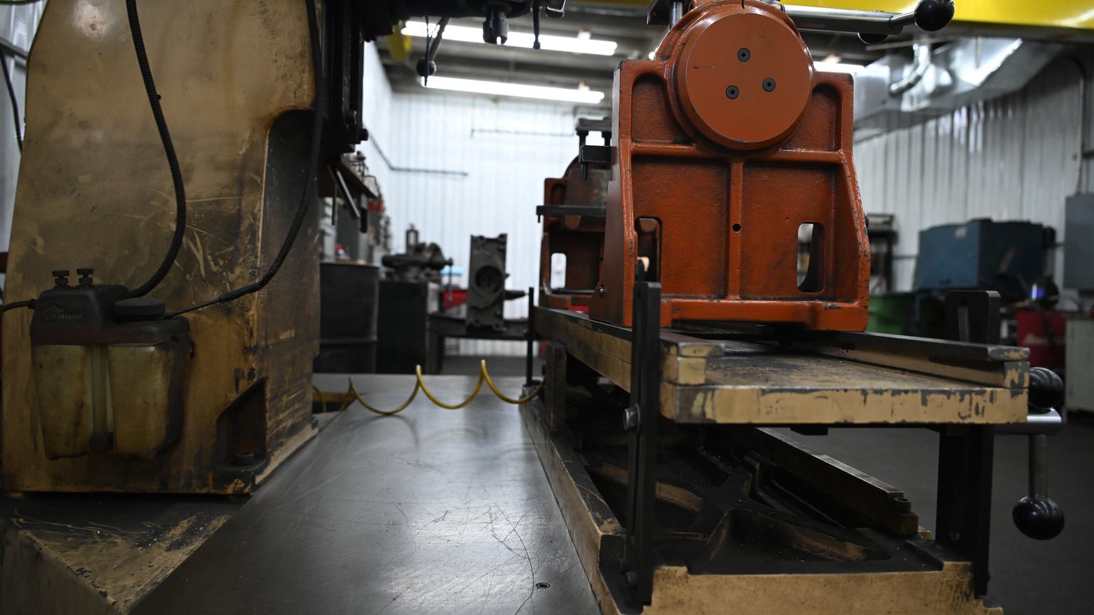 The floor of PDM's machine shop, with a machine base and coolant tank beside a fixture on a steel table.