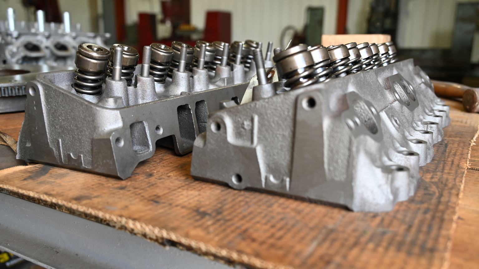 Two assembled cylinder heads with valve springs and retainers installed, resting on a wooden bench.