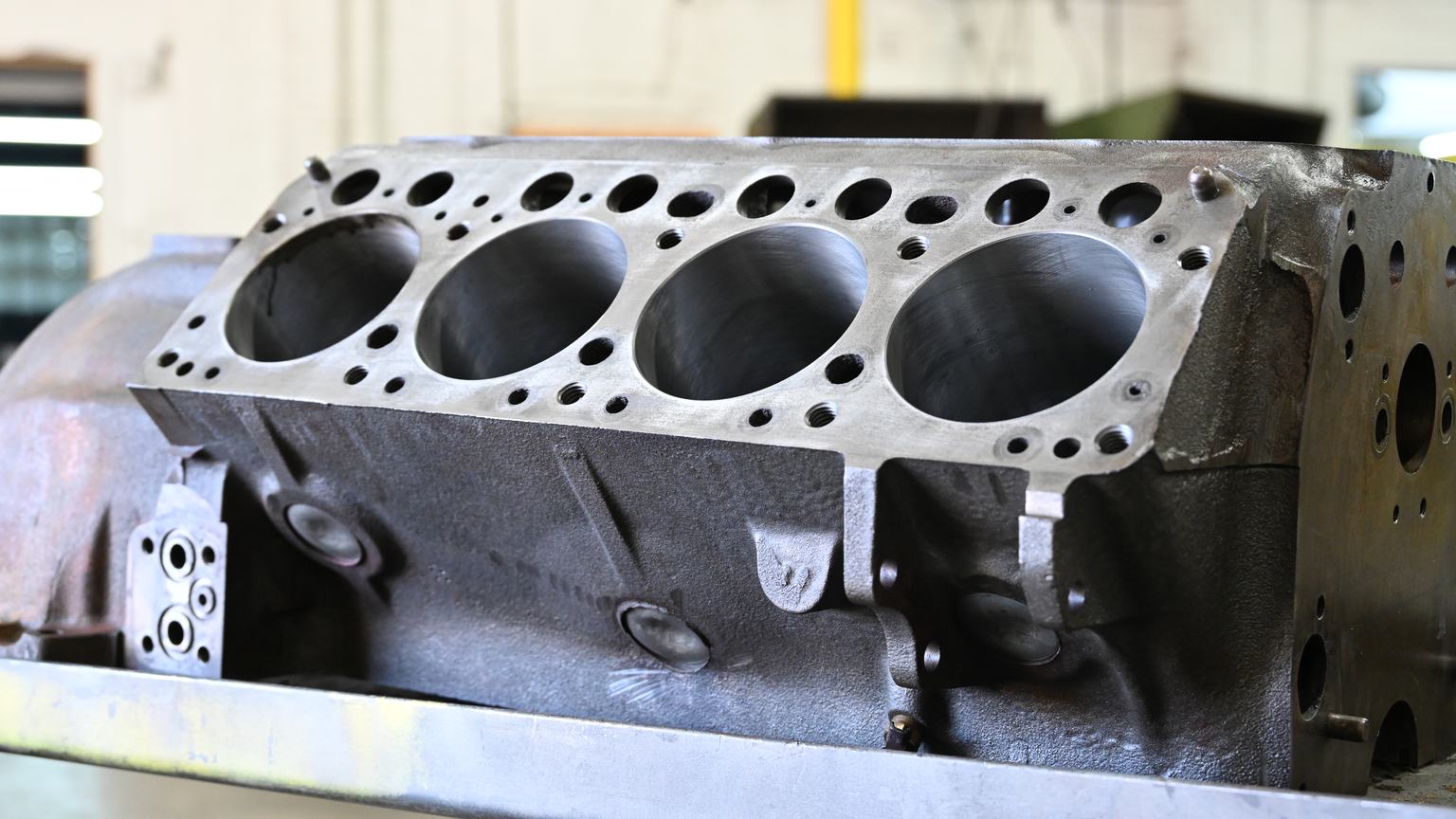 A bare engine block on a stand with four machined cylinder bores and a milled deck surface.