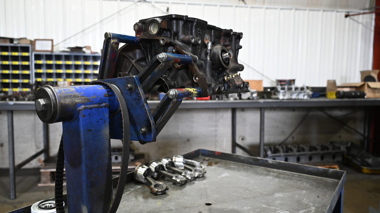 An engine block mounted on a stand with its connecting rods laid out on a cart below.
