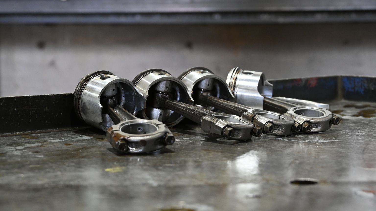 Four pistons attached to connecting rods with bolted rod caps, lined up on a steel bench.